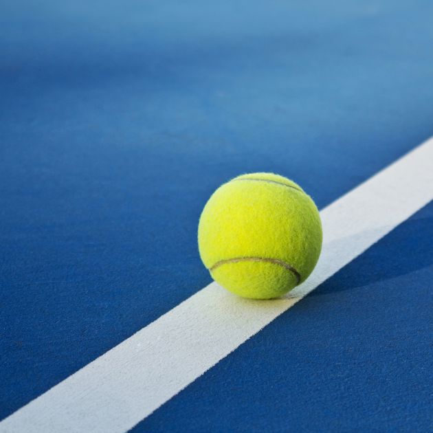 Photo of a yellow tennis ball on a blue court