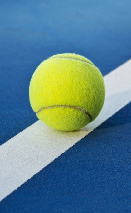 Photo of a yellow tennis ball on a blue court