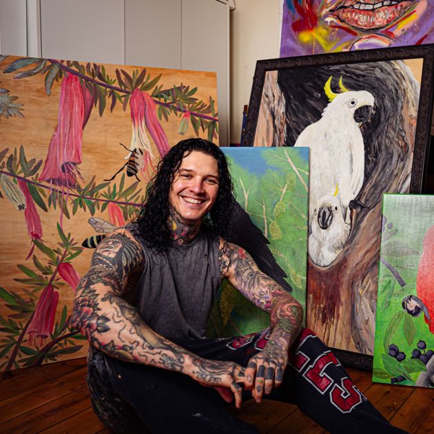 Photo of Indigenous artist Josh Deane sitting in front of his paintings in a studio
